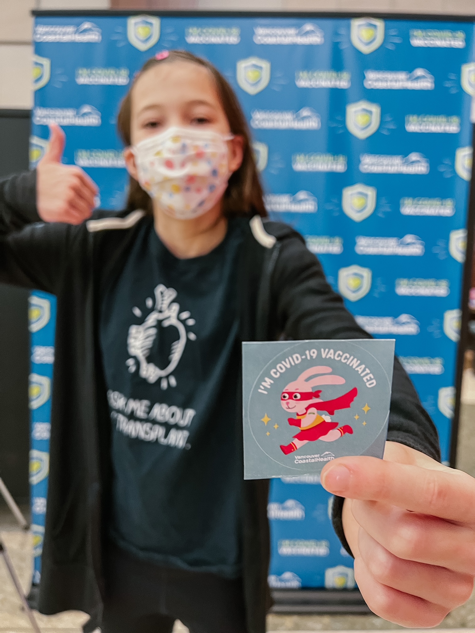 Female child (Addison) wearing a mask holding out an "i'm vaccinated" sticker COVID-19