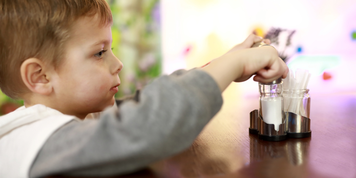 A young boy reaches for a salt shaker on a dining table.