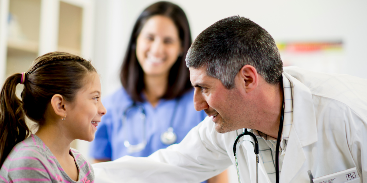 Doctor is looking at a pediatric patient with nurse smiling in background